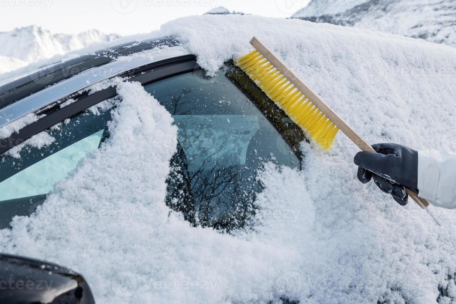 Mano con cepillo para barrer la nieve en el parabrisas del coche foto