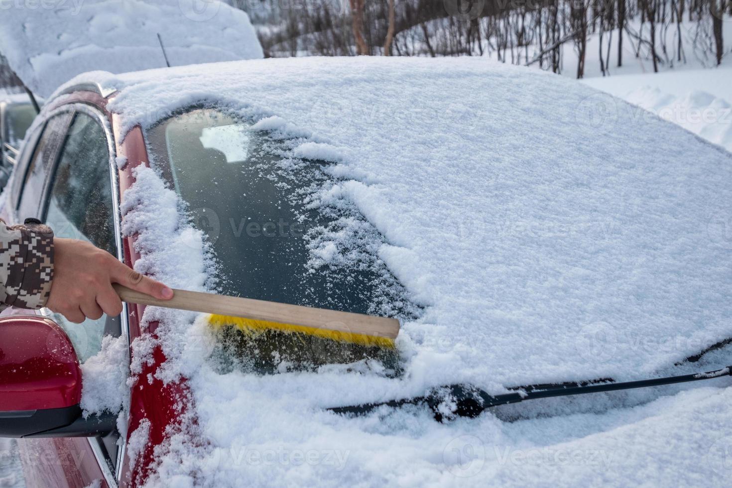 Hand using brush sweeping snow on car windscreen photo