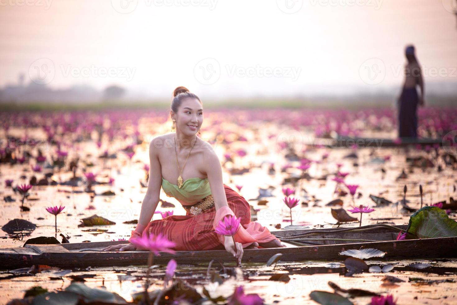 Young Asian women in Traditional dress in the boat and pink lotus flowers in the pond.Beautiful girls in traditional costume.Thai girl in retro Thai dress, Thai girl in traditional dress costume photo