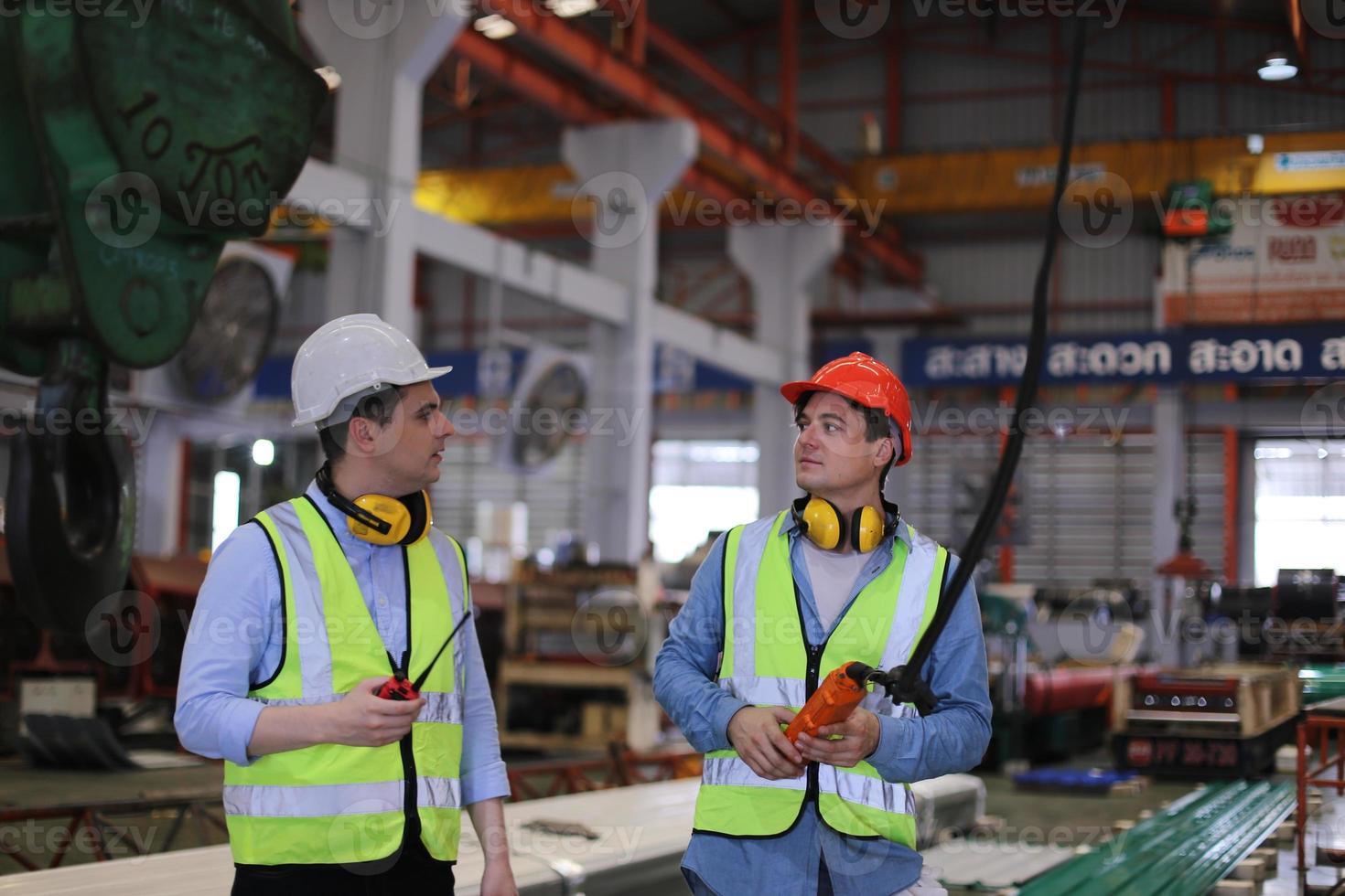 Men industrial engineer wearing a safety helmet while standing in a heavy industrial factory. The Maintenance looking of working at industrial machinery and check security system setup in factory. photo