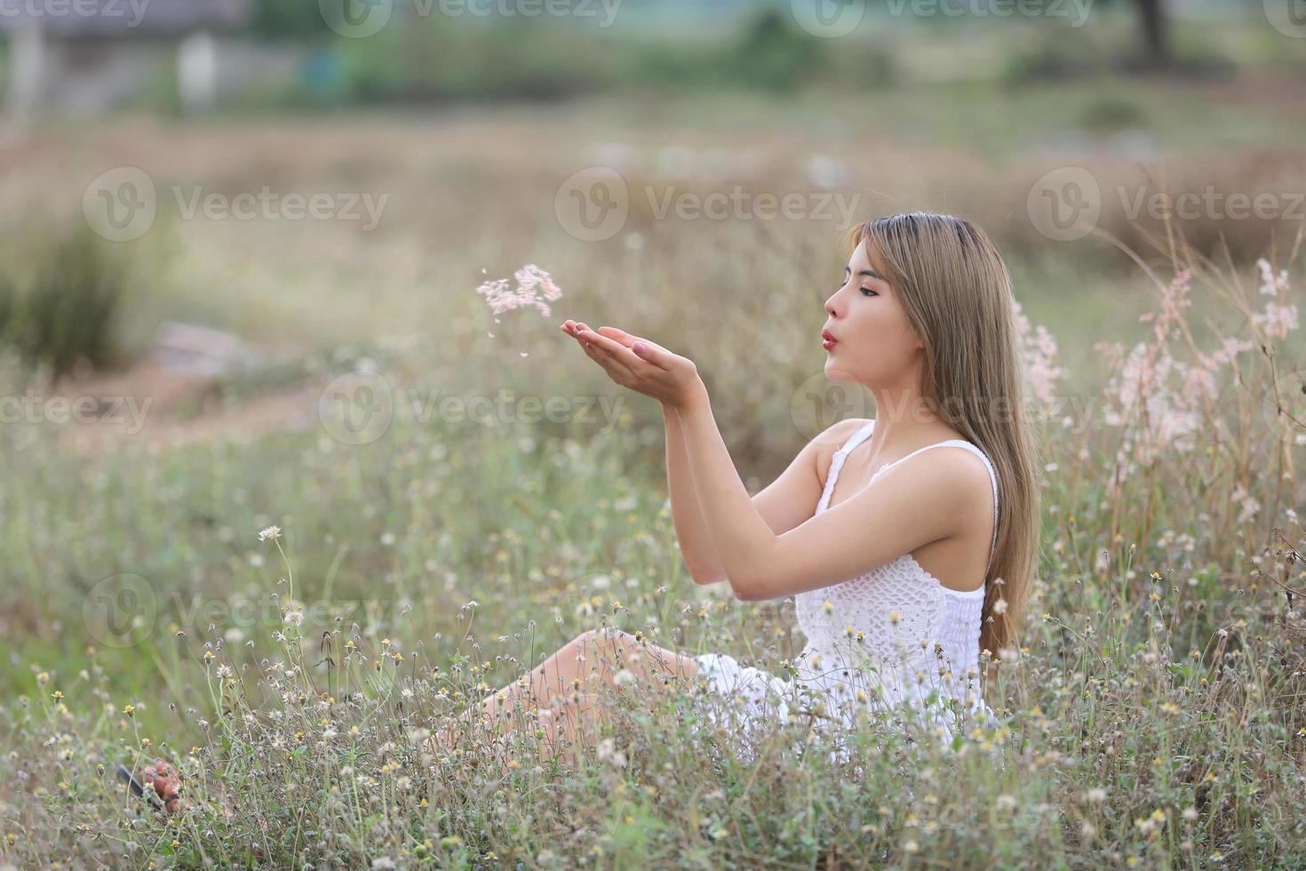 Beautiful Young Woman sitting on the field in green grass and blowing dandelion. Outdoors. Enjoy Nature. Healthy Smiling Girl on spring lawn. Allergy free concept. Freedom photo