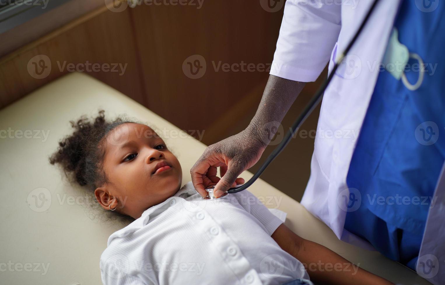 Black skin doctor checking up kid body in clinic. photo