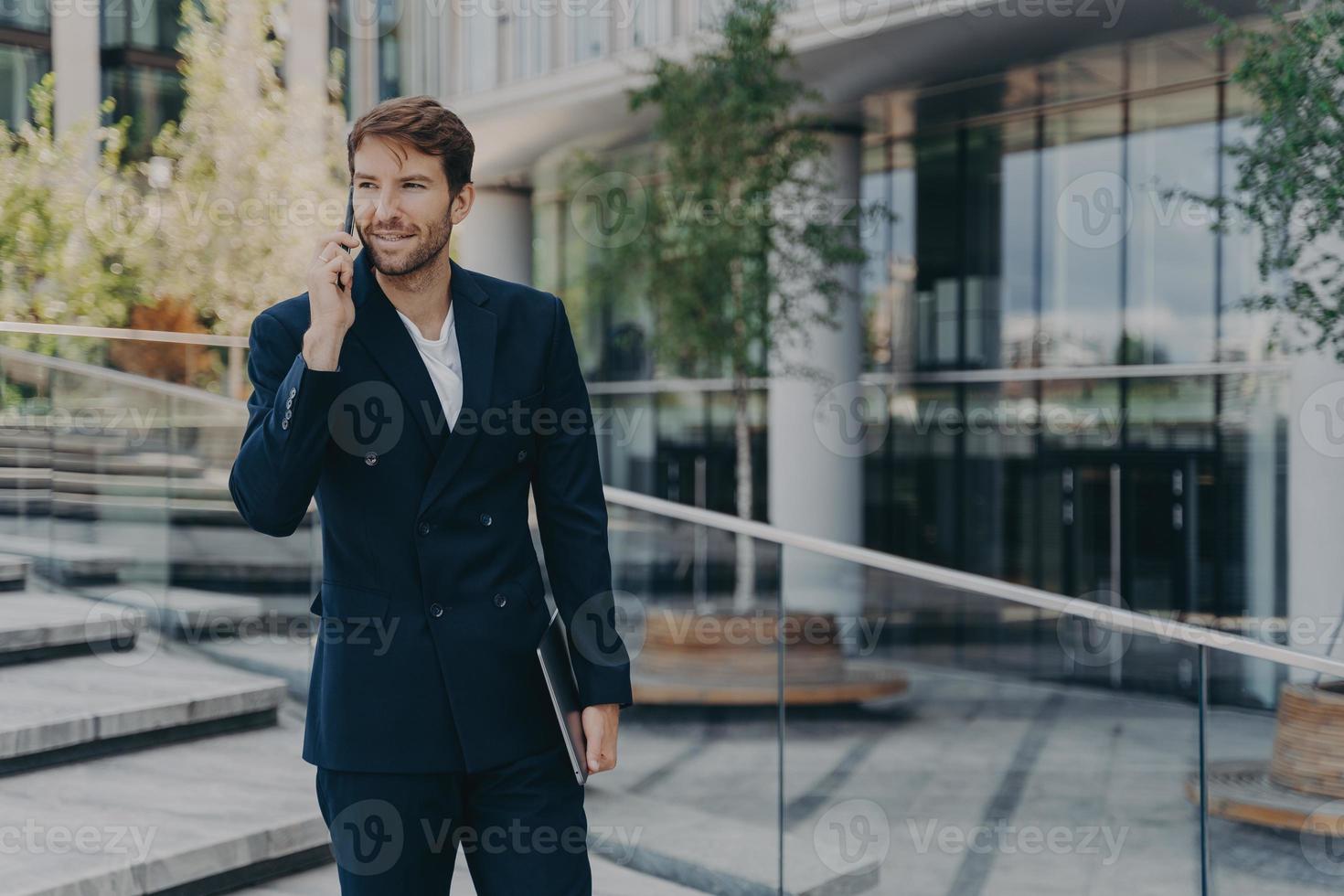 Fashionable unshaven businessman uses modern technologies has telephone conversation holds gadget photo