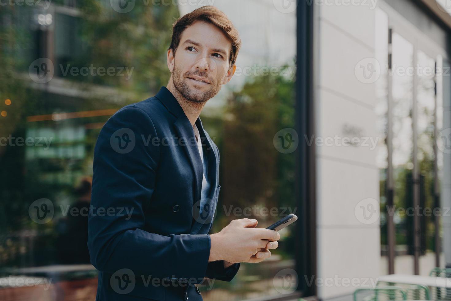 Pensive businessman holds cellular sends text messages dressed formally photo