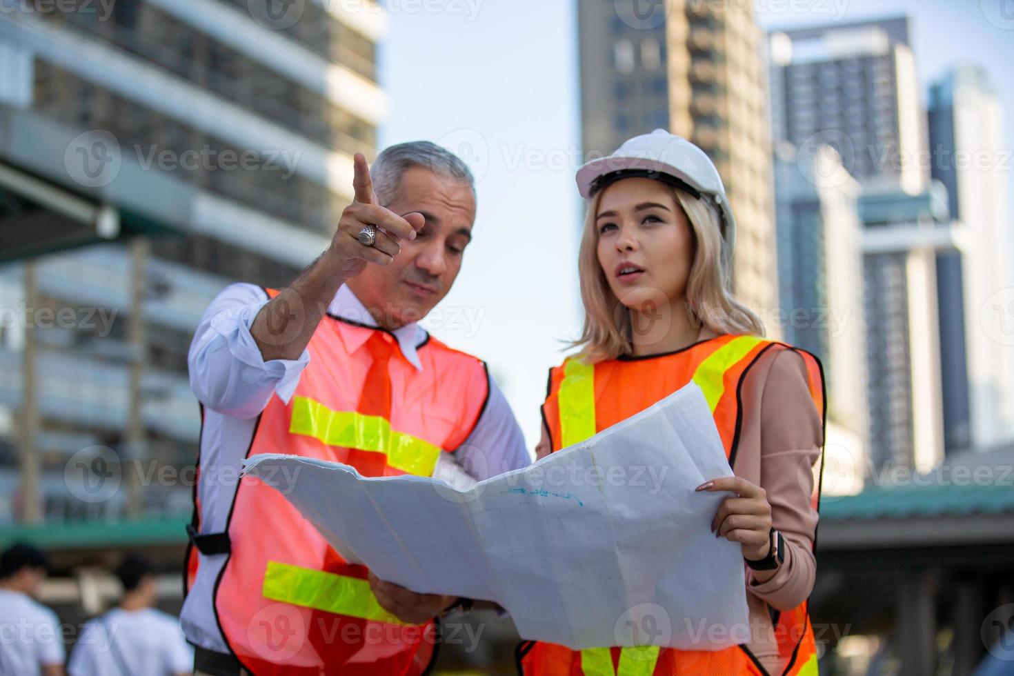 Contractor and architect looking at plan and talking about working on big project. Building in construction process interior. photo