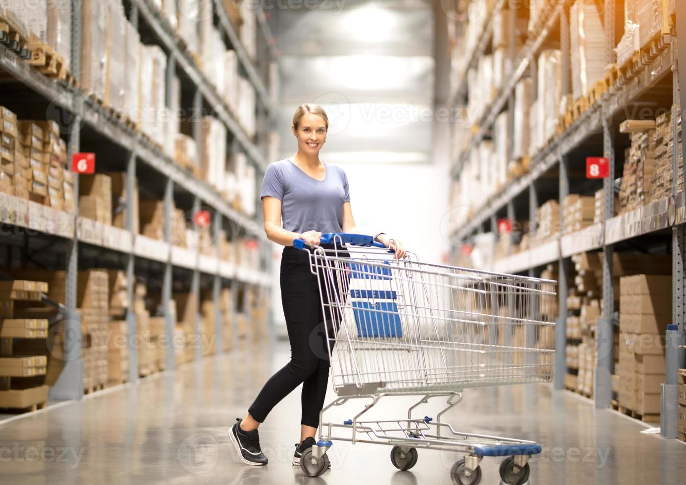 Cheerful woman customer looking up and pulling product on shelf while shopping in hardware store photo