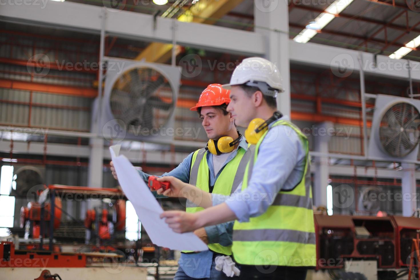 Men industrial engineer wearing a safety helmet while standing in a heavy industrial factory. The Maintenance looking of working at industrial machinery and check security system setup in factory. photo