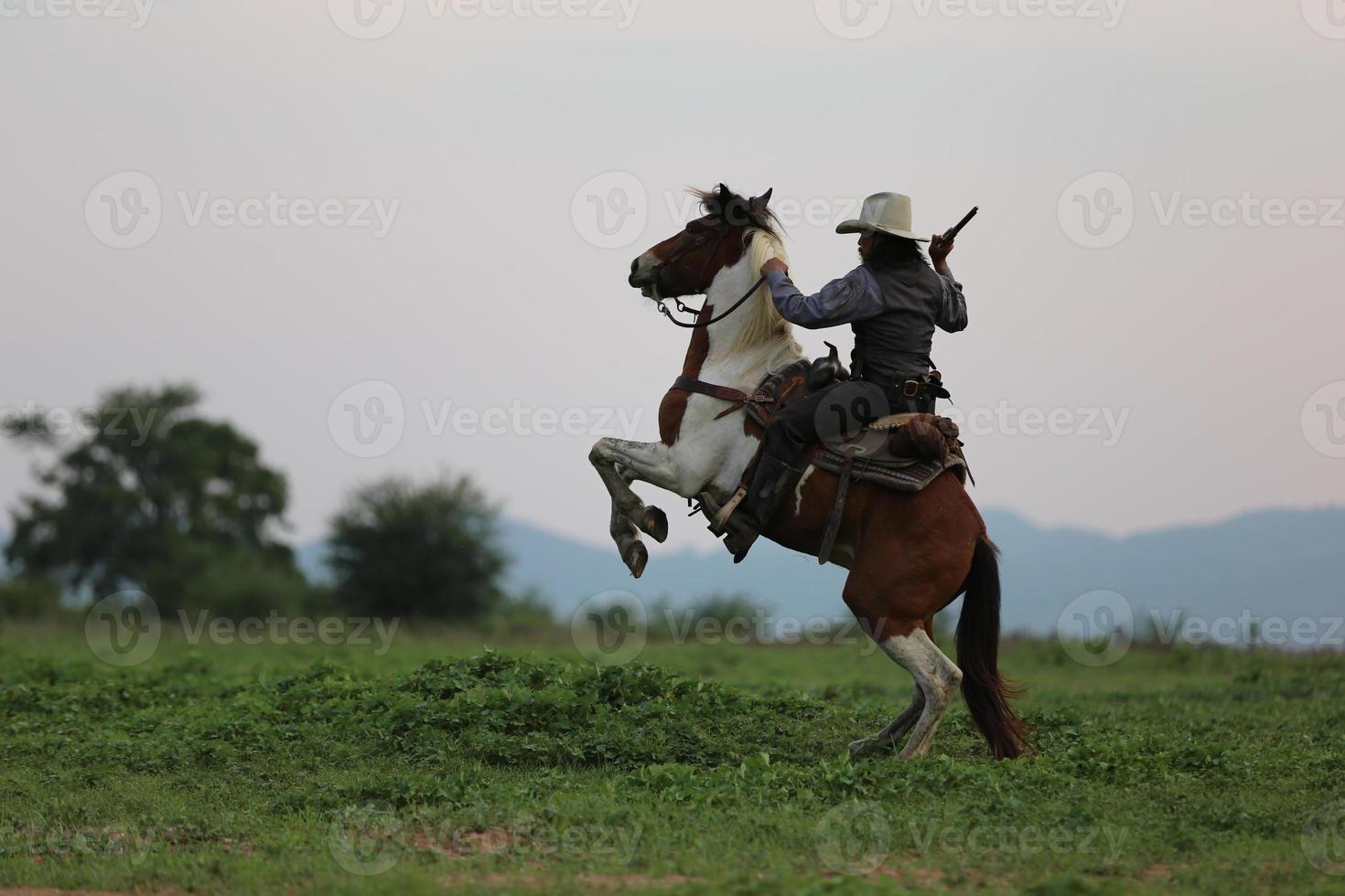 vaquero montando a caballo con la mano sosteniendo un arma contra el fondo del atardecer. foto