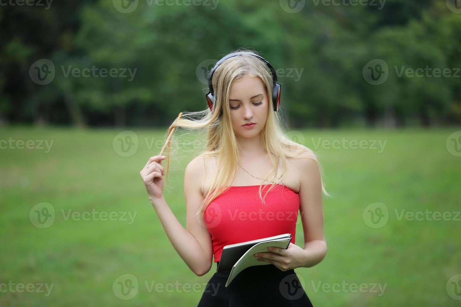 Portrait of young beautiful blonde woman with headphone set standing on the park. photo