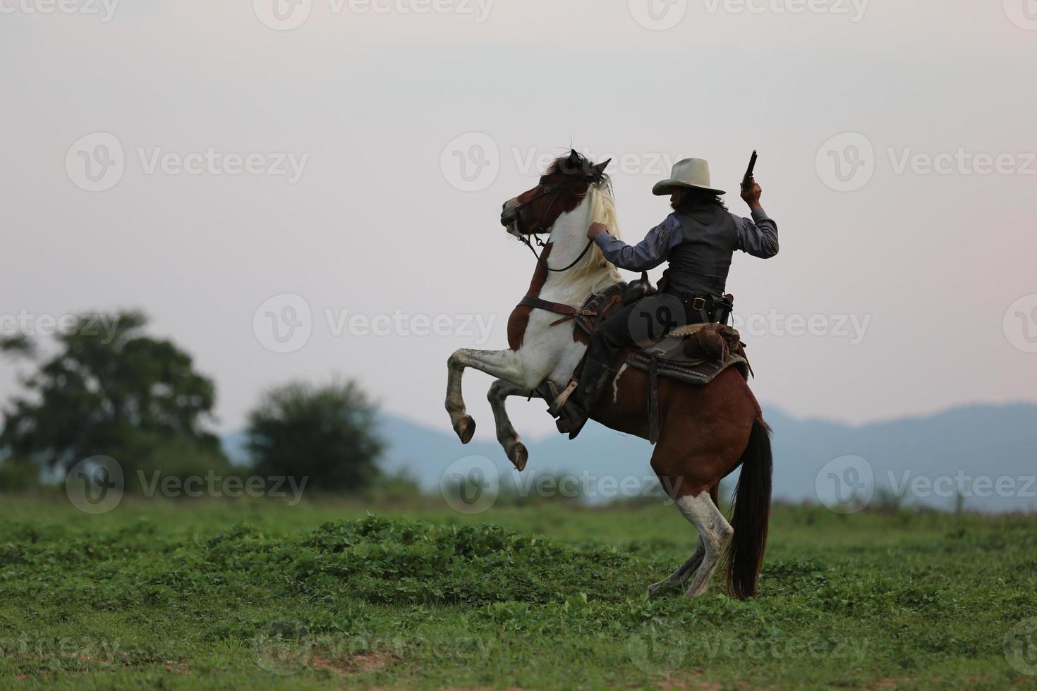 Cowboy riding horse with hand holding gun against sunset background. photo