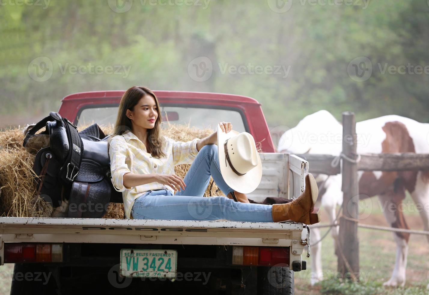 Cowgirl model posing on farm. A portrait of a beautiful young cowgirl leaning against a wall in a stable at farm. photo