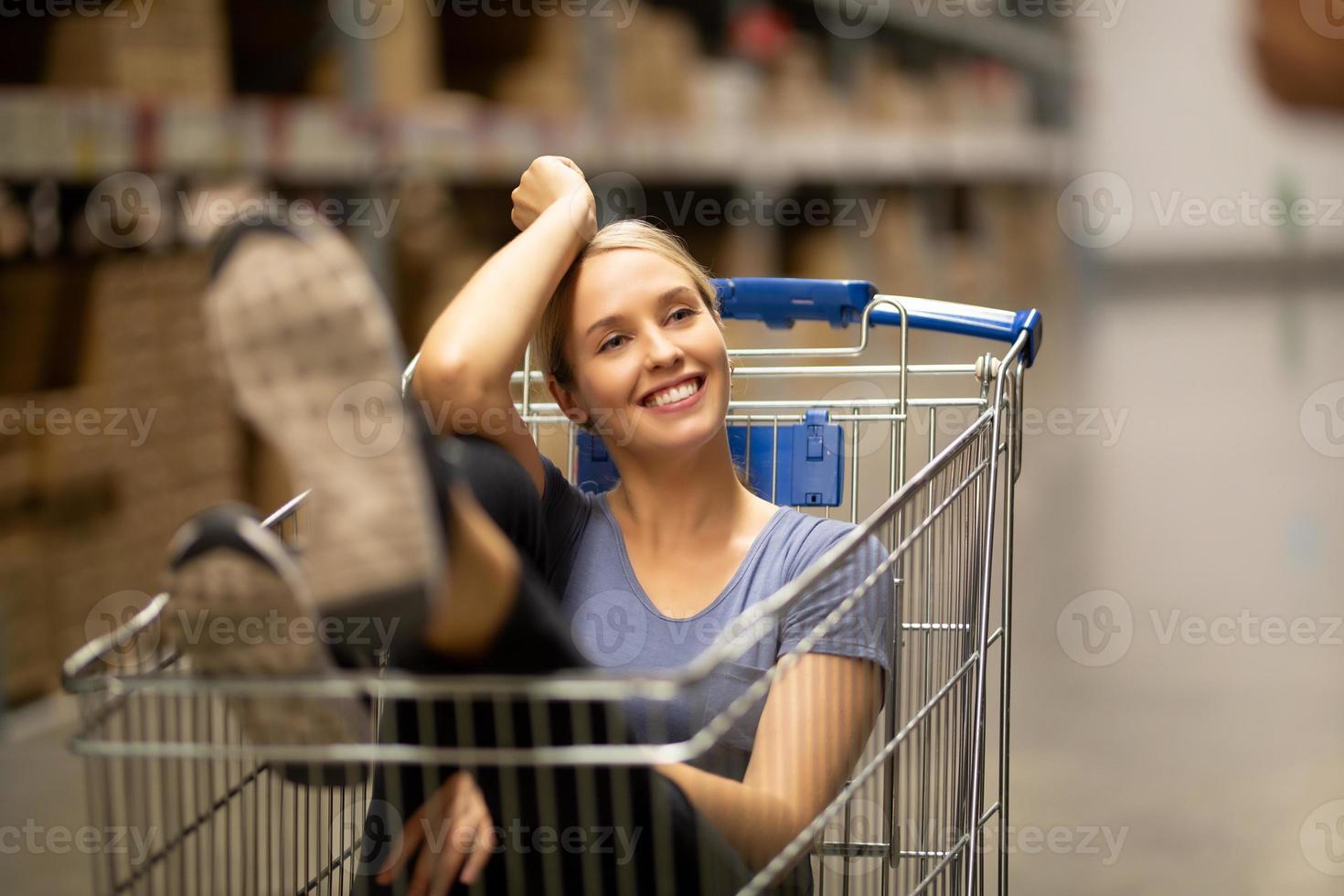 Cheerful woman customer with smiling and looking up while sitting in shopping cart in hardware store photo