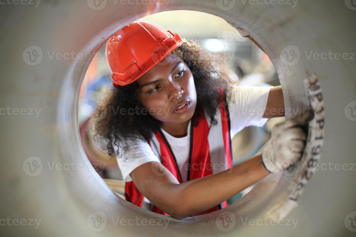 mujer ingeniera industrial que usa un casco de seguridad mientras está de pie en una fábrica industrial pesada. el mantenimiento que busca trabajar en maquinaria industrial y verificar la configuración del sistema de seguridad en fábrica. foto