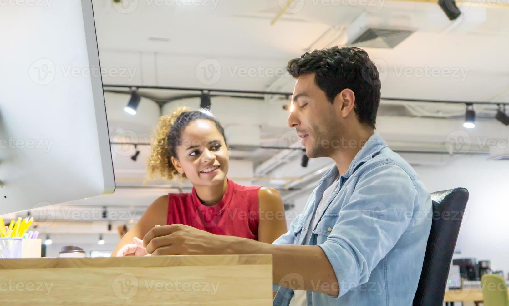 Diverse business colleagues sitting at a desk in a modern office talking together over a computer. photo