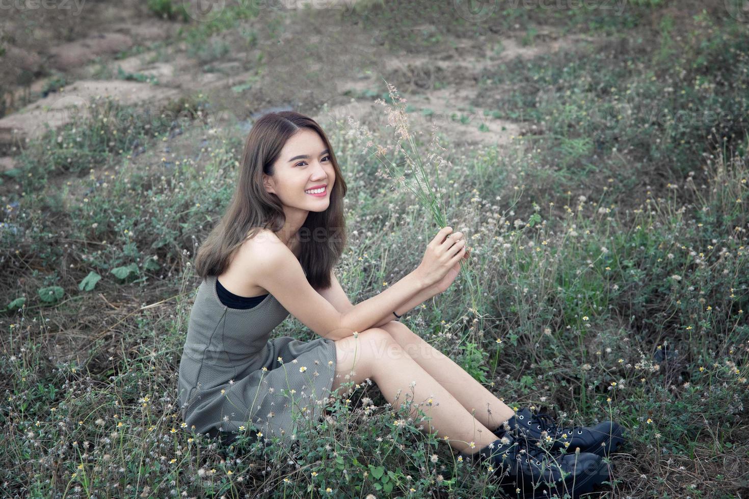 Beautiful Young Woman sitting on the field in green grass and blowing dandelion. Outdoors. Enjoy Nature. Healthy Smiling Girl on spring lawn. Allergy free concept. Freedom photo