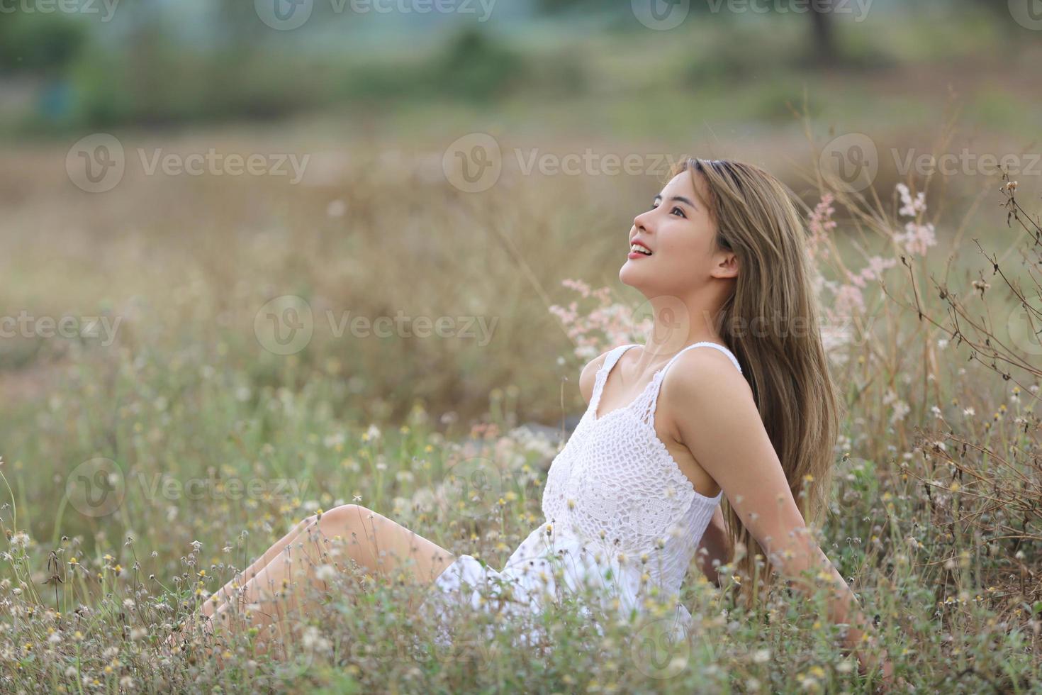 Beautiful Young Woman sitting on the field in green grass and blowing dandelion. Outdoors. Enjoy Nature. Healthy Smiling Girl on spring lawn. Allergy free concept. Freedom photo