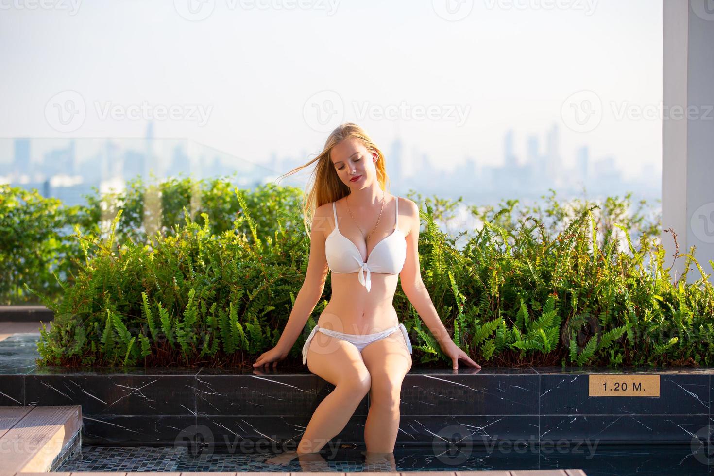 mujer joven disfrutando y relajándose junto a la piscina. modelo de chica joven delgada en bikini blanco junto a la piscina. foto