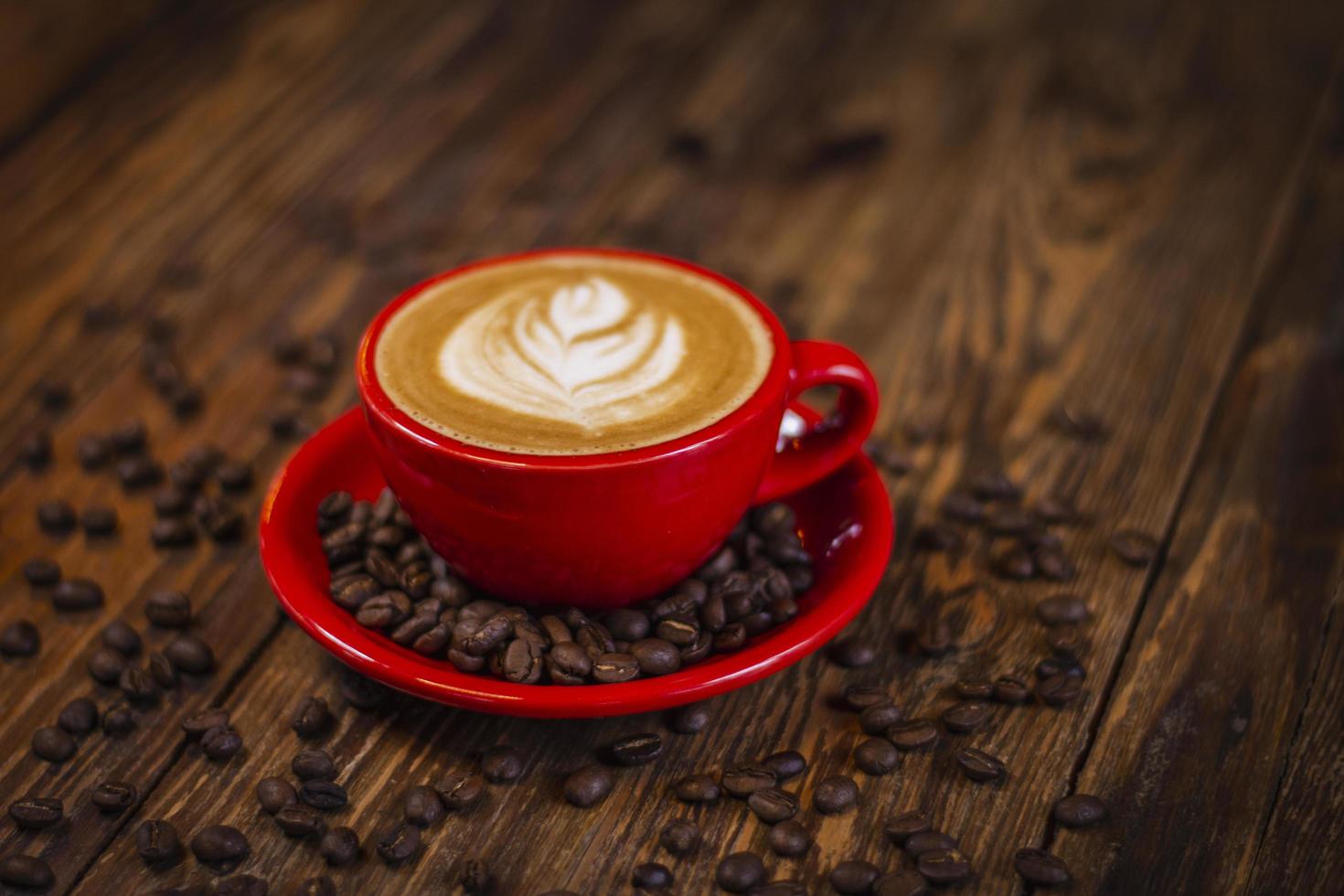 Hot cappuccino coffee in red cup with saucer on wooden table, perspective for text input. photo