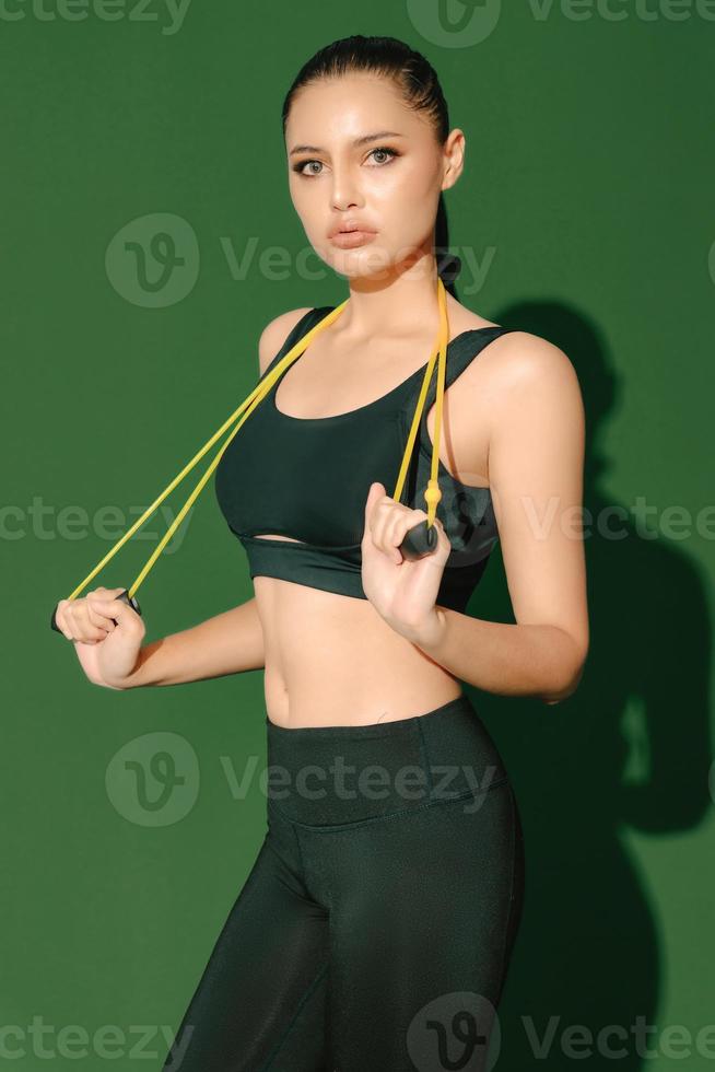 Beautiful strong happy cheerful young Asian sports woman does exercises isolated on green background. Fitness girl in sportswear posing indoors. Movement, Strength and motivation. photo