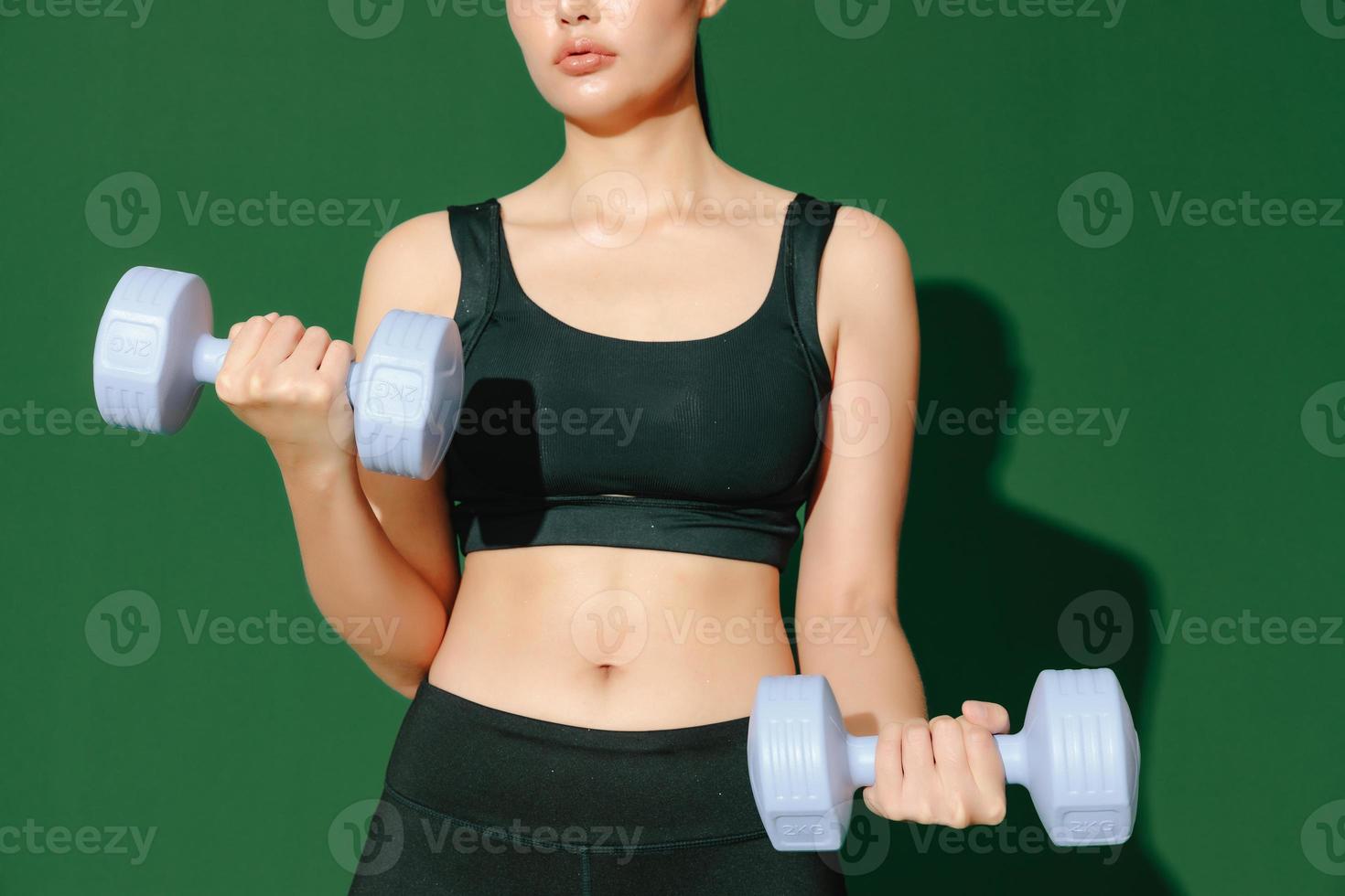 Recortar el cuerpo de cerca de una joven deportista asiática que hace ejercicios aislados en un fondo verde. chica fitness en ropa deportiva posando en el interior. movimiento, fuerza y motivación. foto
