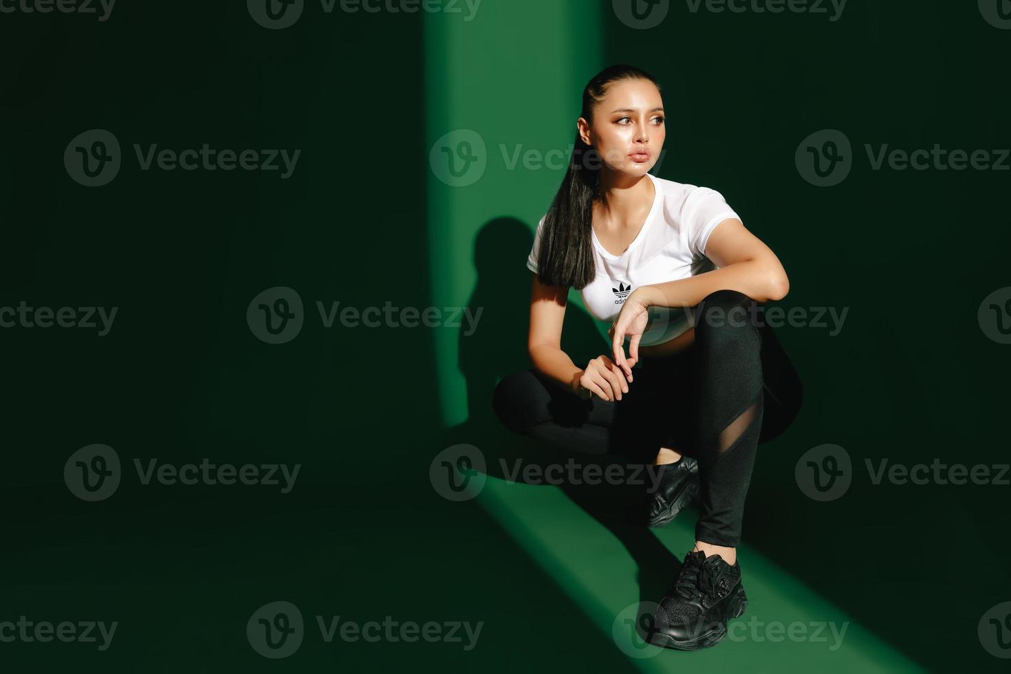 Beautiful strong happy cheerful young Asian sports woman does exercises isolated on green background. Fitness girl in sportswear posing indoors. Movement, Strength and motivation. photo