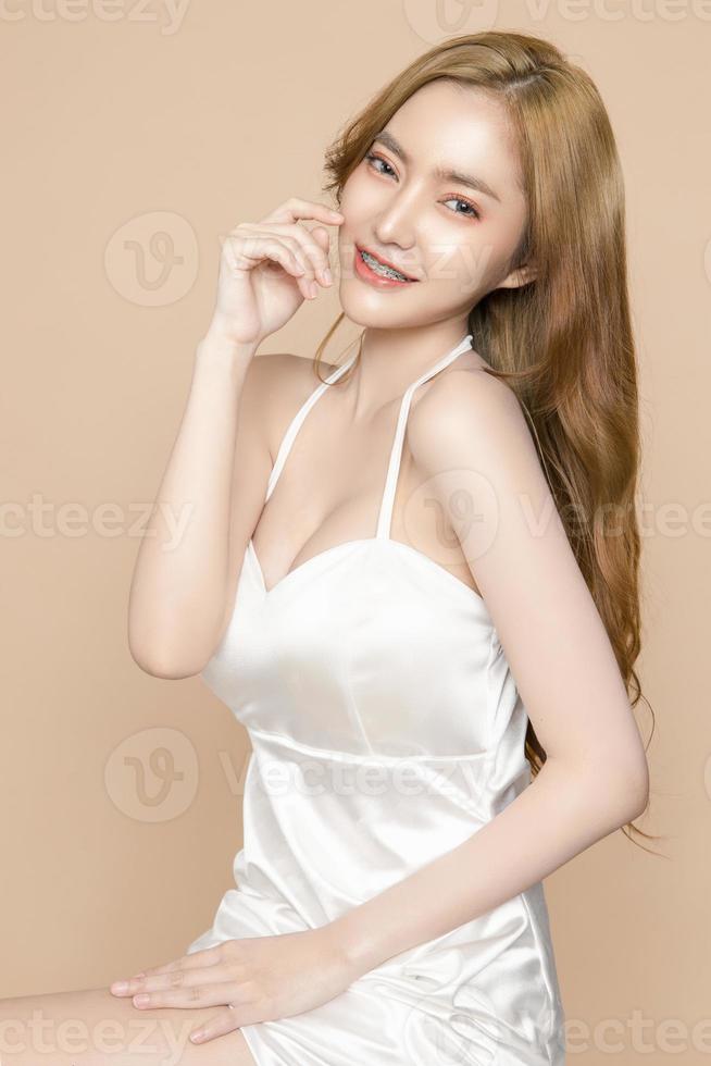 Cute young Asian woman wearing braces is feeling happy with clean fresh skin isolated over cream background. Plastic surgery Face care, Facial treatment, Cosmetology, beauty and spa, Women portrait. photo