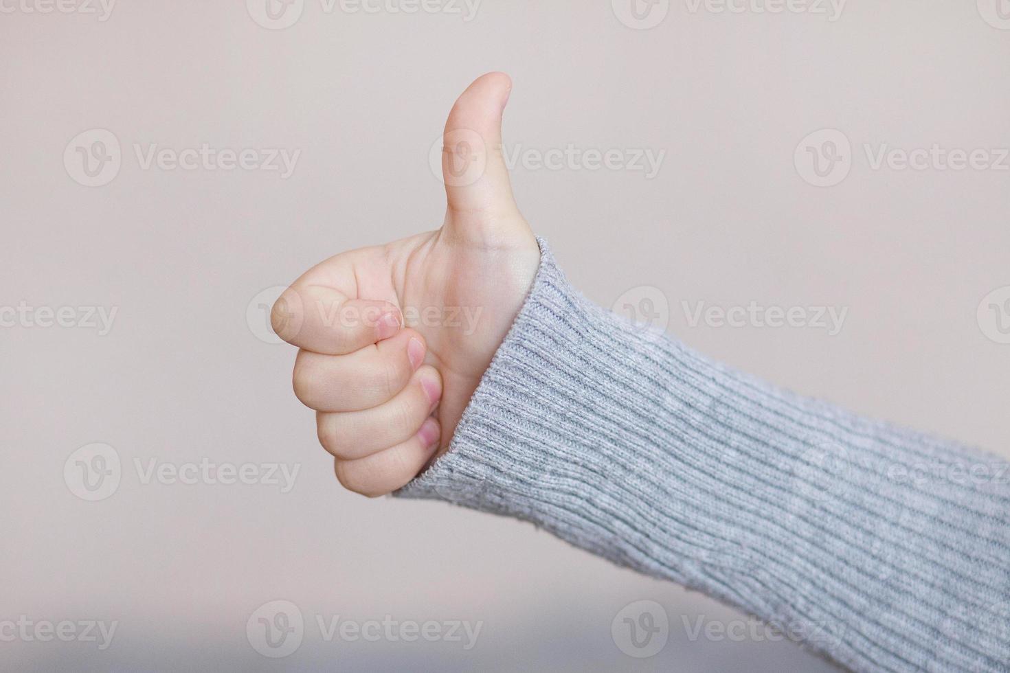 close-up photo of a child's hand of a girl showing a thumbs up sign on a light background.Thumbs up. A child's hand shows the like