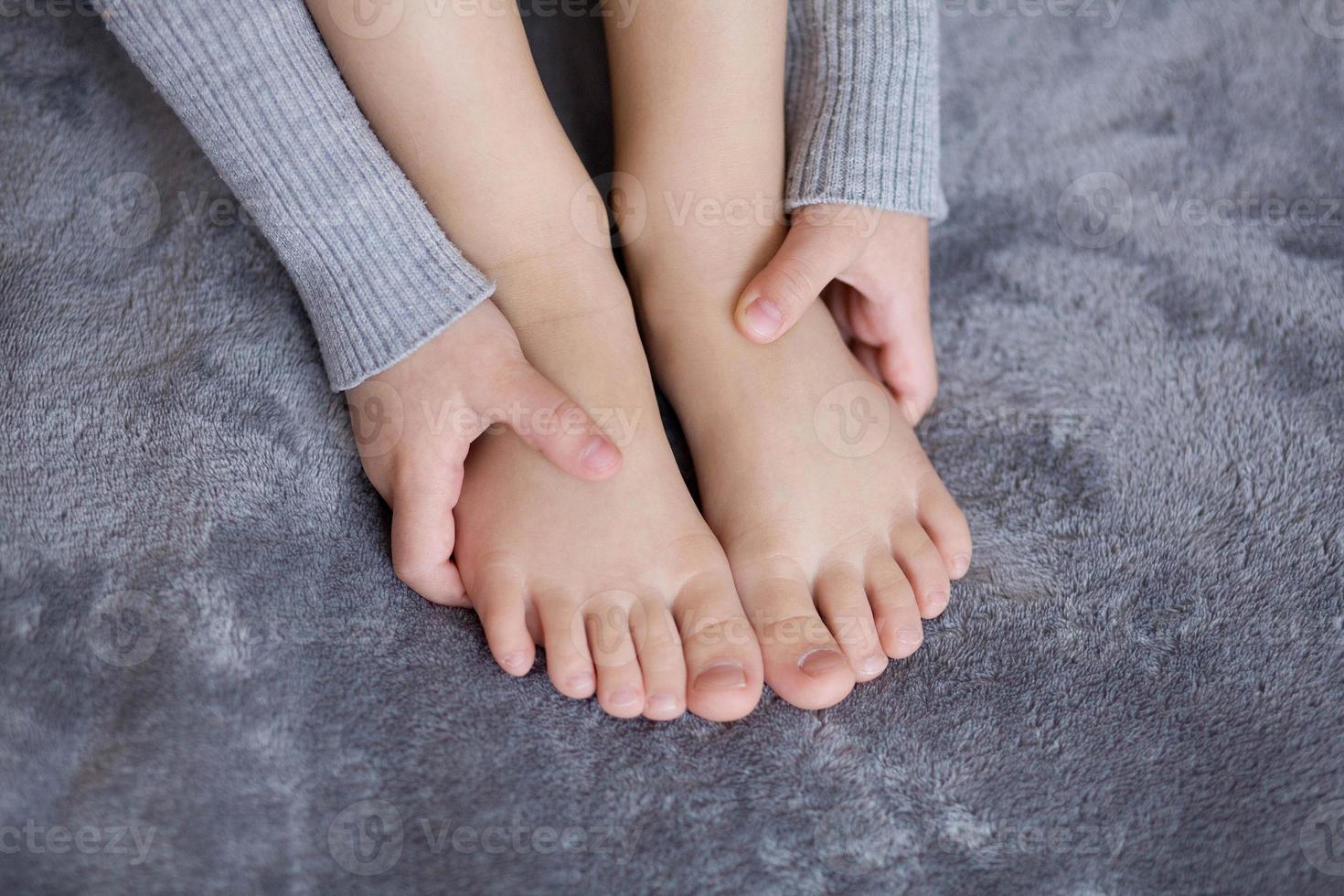 A girl in a gray dress holds her legs with her hands on a gray background, close-up. Children's games, girl photo