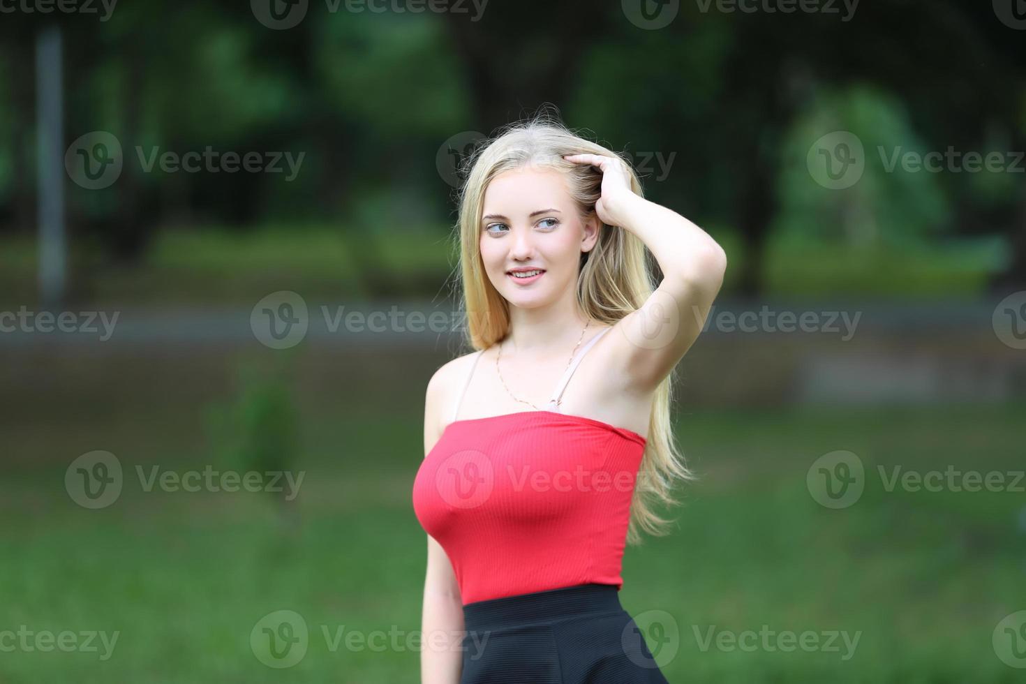 hermosa mujer rubia de pie mientras escucha música en los auriculares en el parque. foto