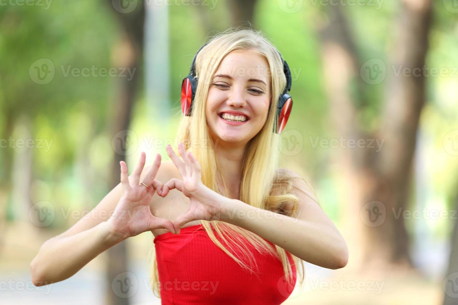 Beautiful blonde woman standing while listening music on headphone at park. photo