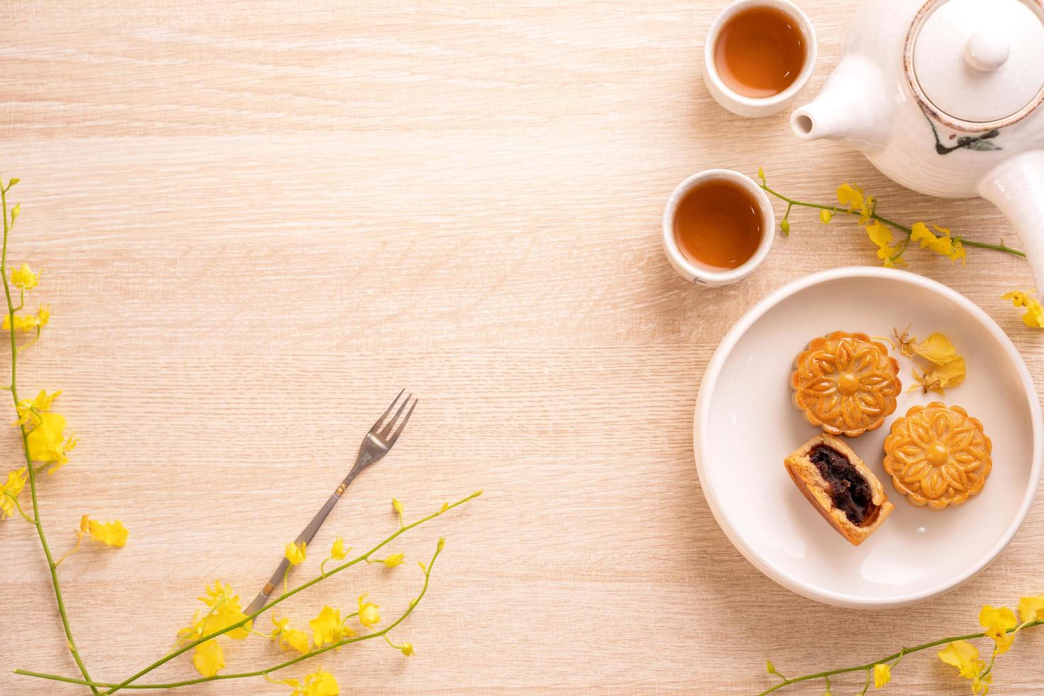 Tasty moon cake for Mid-Autumn festival on bright wooden table, concept of festive afternoon tea decorated with yellow flowers, top view, flat lay. photo