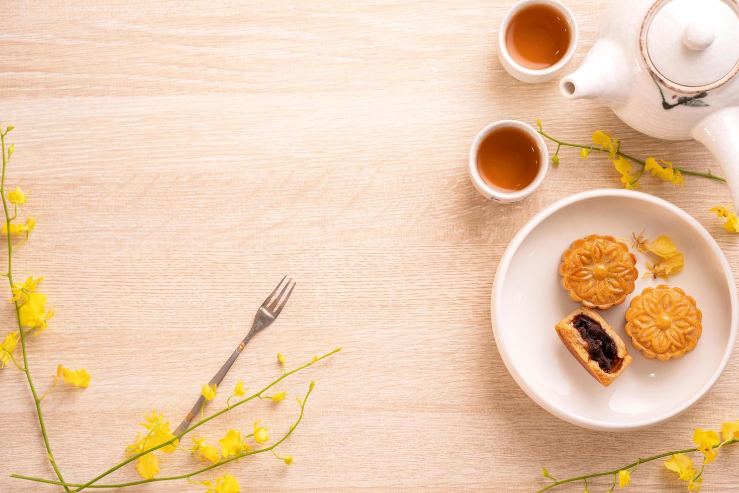 sabroso pastel de luna para el festival de mediados de otoño en una mesa de madera brillante, concepto de té festivo decorado con flores amarillas, vista superior, puesta plana. foto