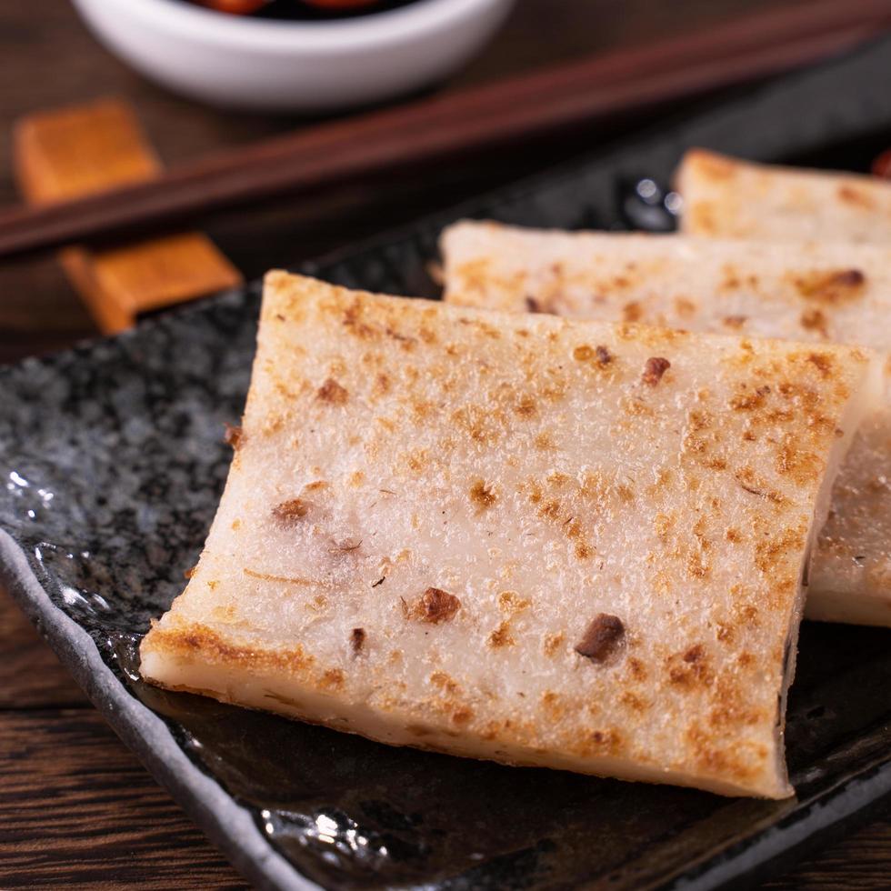 Delicious turnip cake, Chinese traditional local dish radish cake in restaurant with soy sauce and chopsticks, close up, copy space. photo