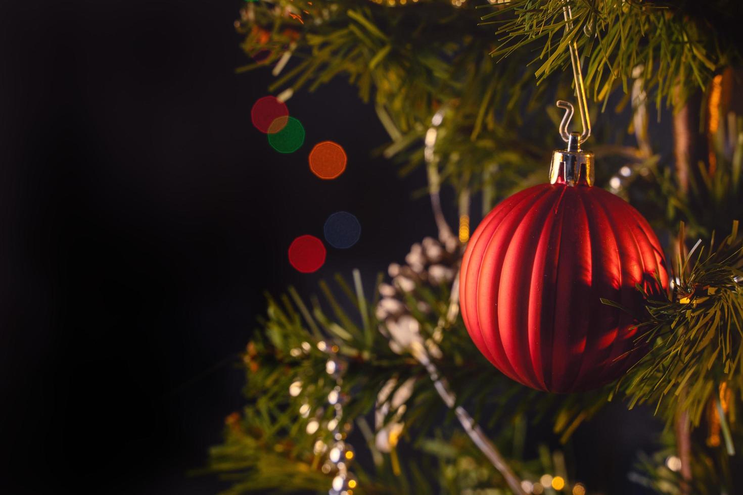 bello concepto de decoración navideña, adorno colgado en el árbol de navidad con punto de luz brillante, fondo negro oscuro borroso, detalle macro, primer plano. foto