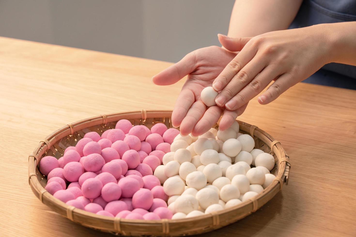 An Asia woman is making Tang yuan, yuan xiao, Chinese traditional food rice dumplings in red and white for lunar new year, winter festival, close up. photo