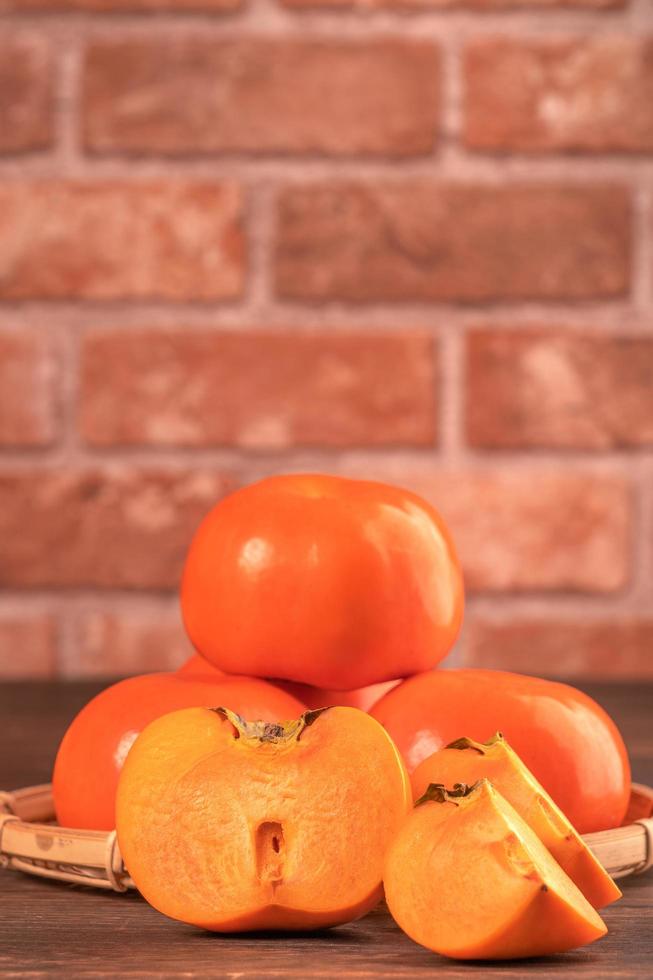 Fresh beautiful sliced sweet persimmon kaki on dark wooden table with red brick wall background, Chinese lunar new year fruit design concept, close up. photo