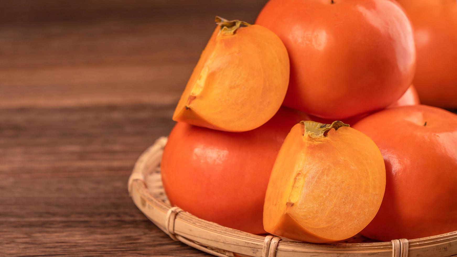 Fresh beautiful sliced sweet persimmon kaki on dark wooden table with red brick wall background, Chinese lunar new year fruit design concept, close up. photo