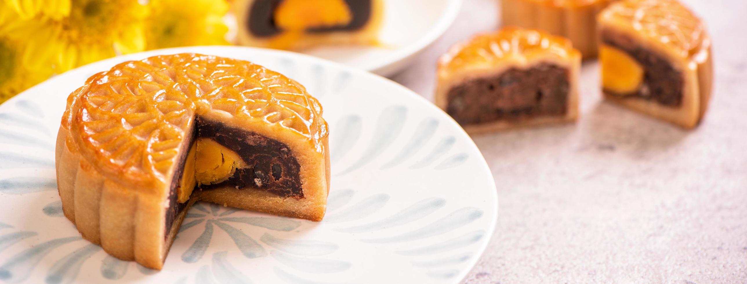 Mid-Autumn Festival traditional food concept - Beautiful cut moon cake on blue pattern plate on white background with flower, close up, copy space photo