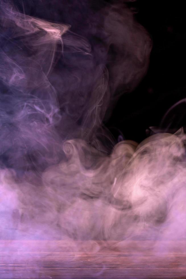 Conceptual image of multi-colored smoke isolated on dark black background and wooden table. photo