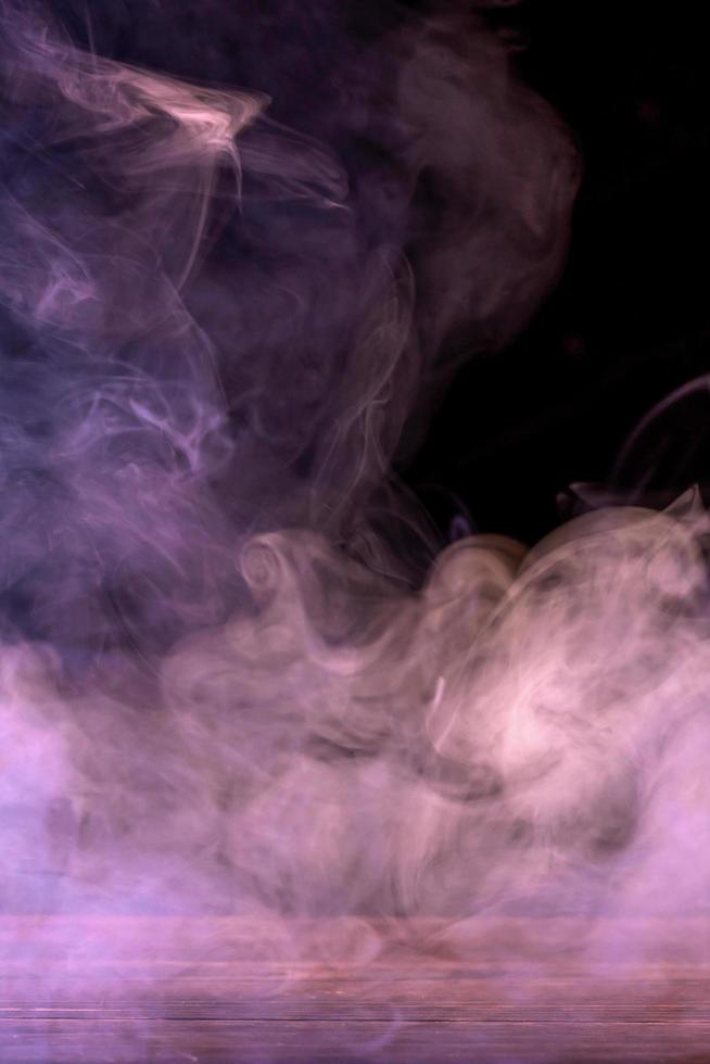 Conceptual image of multi-colored smoke isolated on dark black background and wooden table. photo