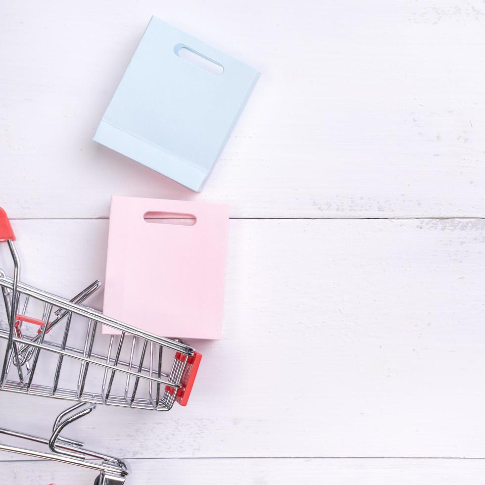 Abstract design element,annual sale,shopping season concept,mini cart with colorful paper bag on white wooden table background,top view,flat lay photo