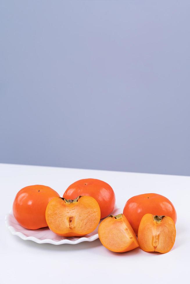 Fresh beautiful sliced sweet persimmon kaki isolated on white kitchen table with gray blue background, Chinese lunar new year design concept, close up. photo