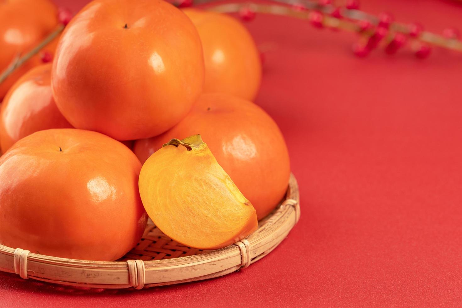 Fresh beautiful sliced sweet persimmon kaki isolated on red table background and bamboo sieve, Chinese lunar new year design concept, close up. photo