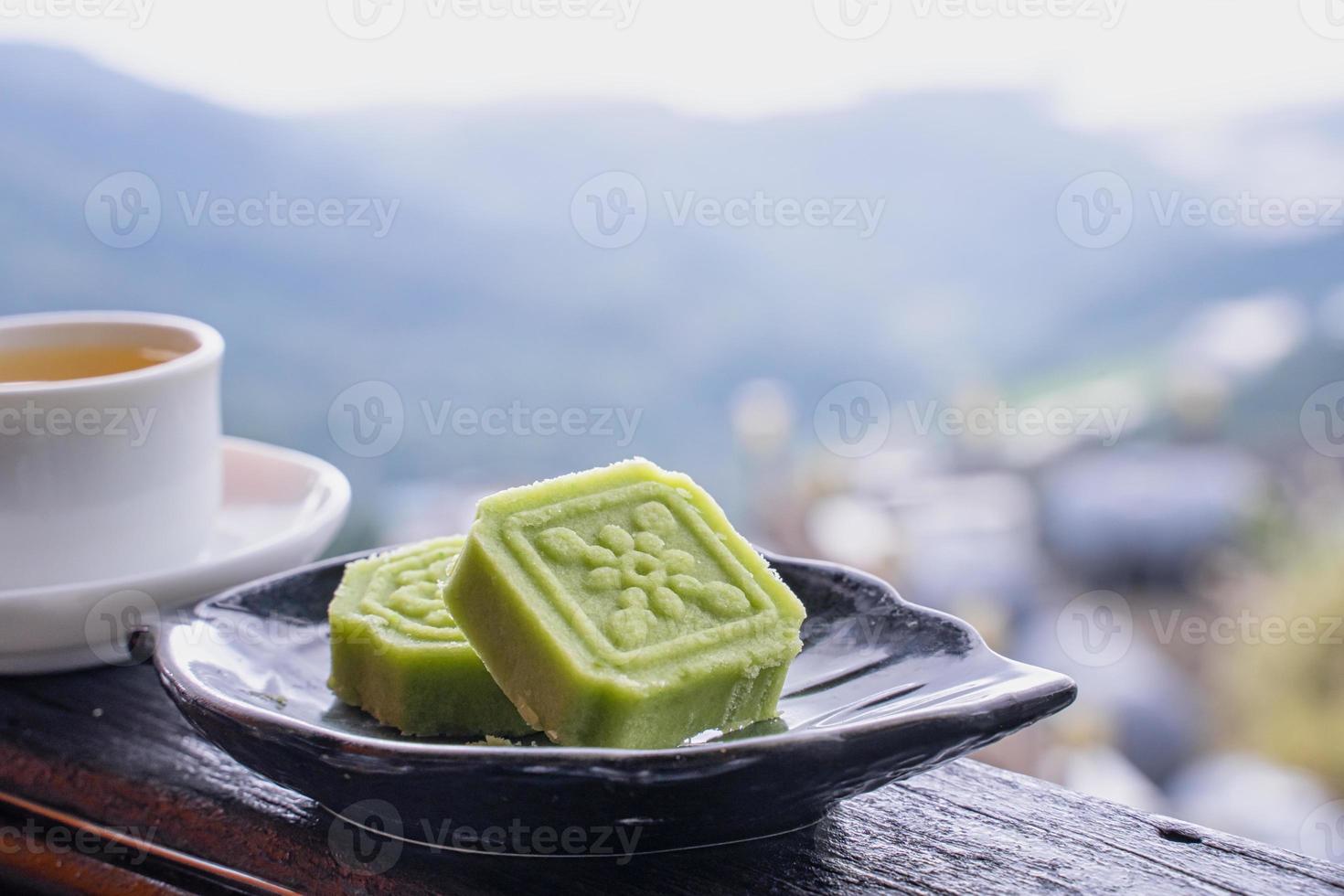 Delicious green mung bean cake with black tea plate on wooden railing of a teahouse in Taiwan with beautiful landscape in background, close up. photo