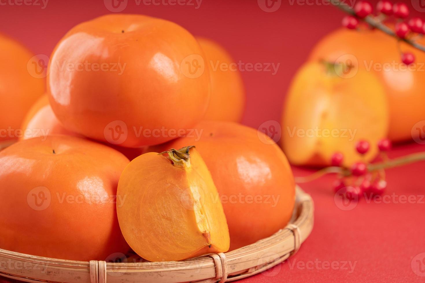 Fresh beautiful sliced sweet persimmon kaki isolated on red table background and bamboo sieve, Chinese lunar new year design concept, close up. photo