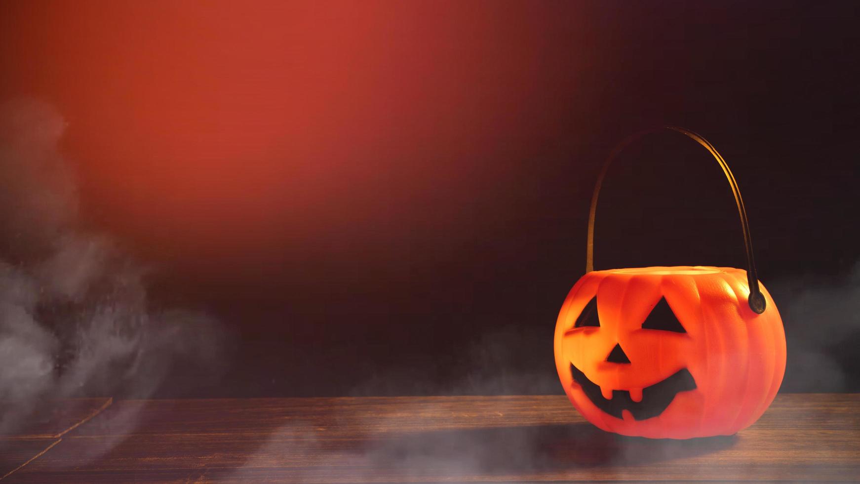 concepto de halloween - linterna de calabaza de plástico naranja sobre una mesa de madera oscura con una luz brillante borrosa en el fondo, truco o trato, de cerca. foto