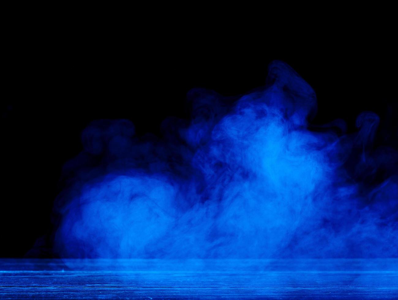 Conceptual image of blue smoke isolated on dark black background and wooden table. photo