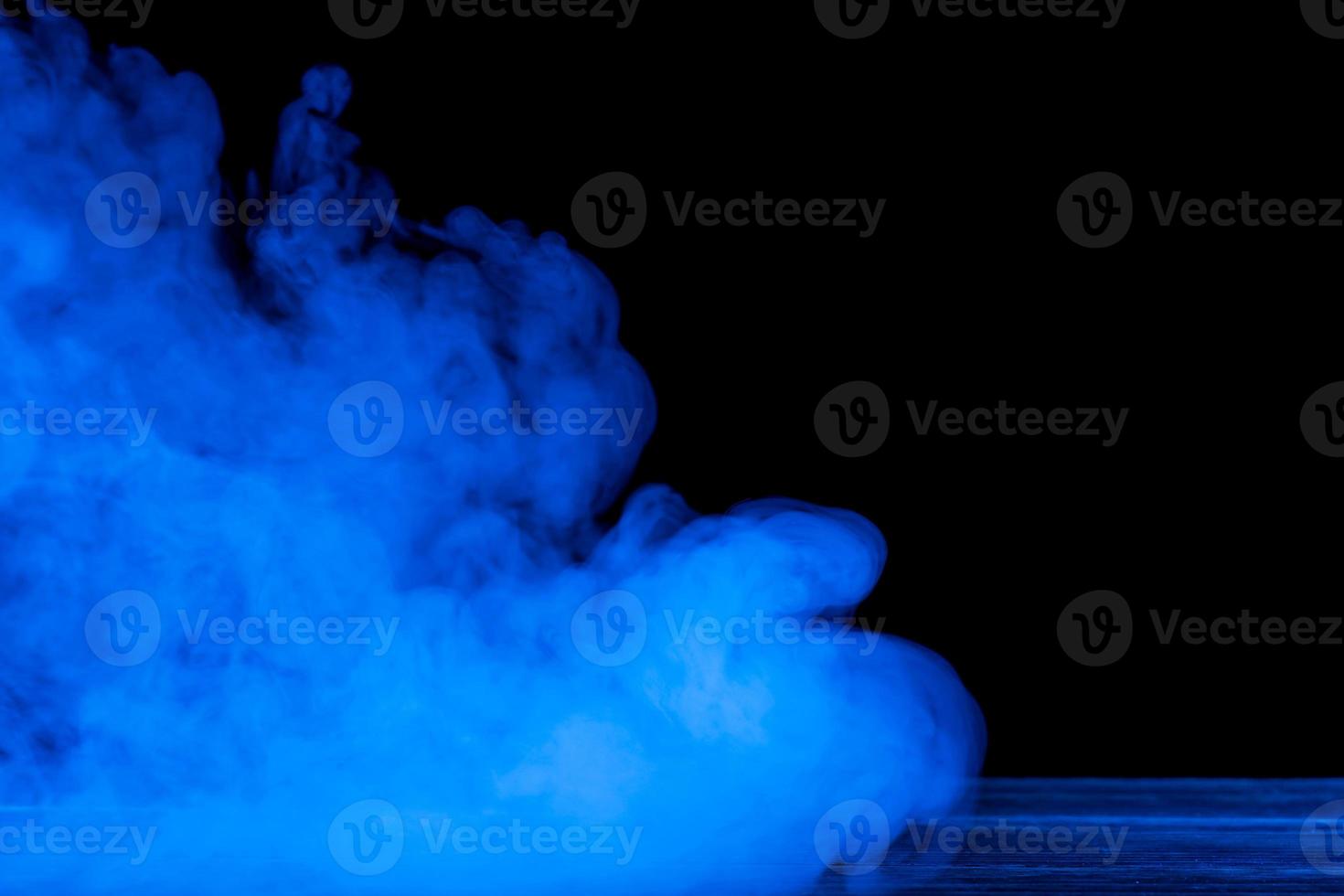 Conceptual image of blue smoke isolated on dark black background and wooden table. photo