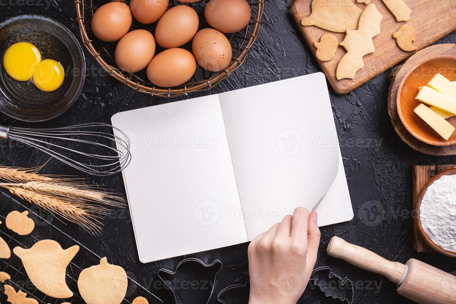 Woman is reading cookbook recipe of making Halloween cookies with baking ingredients, design concept of cooking class, top view, flat lay, overhead. photo