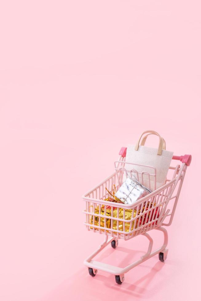 concepto de temporada de compras de venta anual - mini carrito de compras rosa lleno de regalo de bolsa de papel aislado en fondo rosa pálido, espacio de copia en blanco, primer plano foto